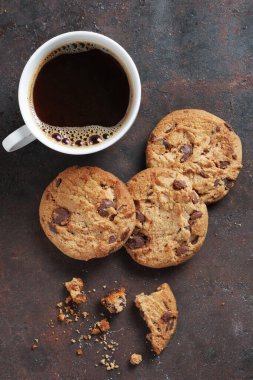 Paslı metal arka planda bir fincan kahve ve çikolatalı kurabiye.