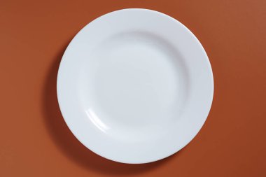 Kahverengi zemin üzerinde boş beyaz seramik plaka, üst görünüm