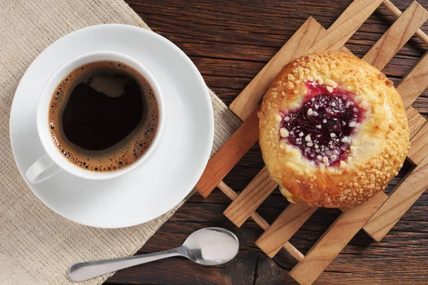 Bun with jam and cup of coffee for breakfast on rustic table close-up, top view