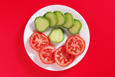 Kırmızı arka planda salatalık ve domates dilimleri.