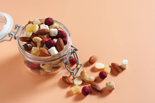 Mixture of nuts and candied fruits in glass jar on a beige background. Copy space
