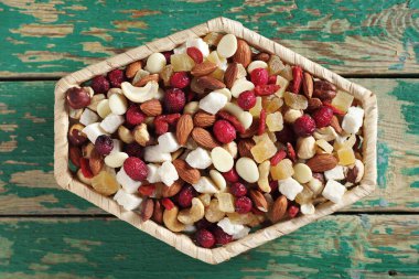 Çeşit çeşit fındık ve kuru meyveler hasır kasede eski yeşil ahşap arka planda, üst manzara