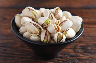 Ahşap masadaki siyah kasede fıstıklı fındıklı yakın plan.