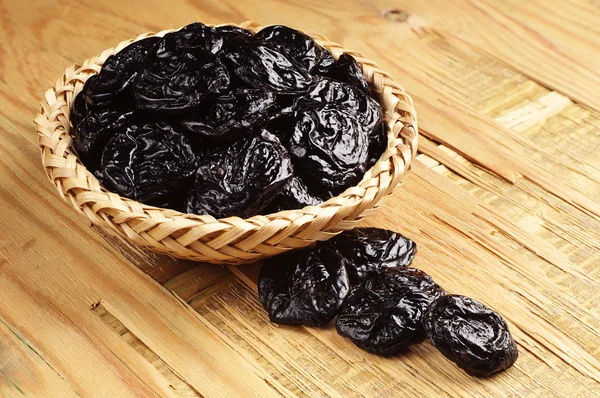 Prunes in a wicker bowl and near — Stock Photo, Image