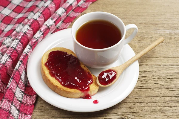 Šálek čaje a buchta s jahodovou marmeládou — Stock fotografie