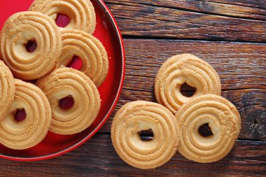 Kırmızı bir plaka üzerinde gevrek girdap kurabiyelerinin üst görüntüsü ve kopyalama alanı olan ahşap zemin.