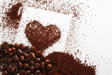 Beyaz arka planda kavrulmuş fasulye ile kalp şeklinde öğütülmüş kahve..