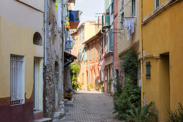 Sunny narrow street with colorful old buildings and green potted plants in medieval town Villefranche-sur-Mer on French Riviera, France.