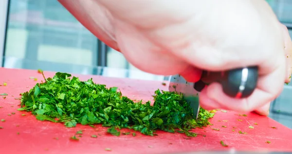 Male chef cutting parsley with big knife on red chopping board — Stock Photo, Image