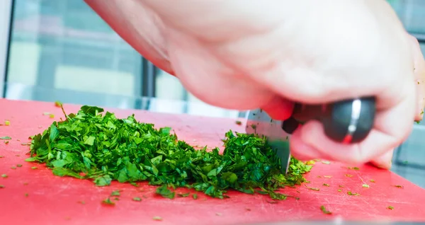 Prezzemolo da taglio chef maschio con coltello grande sul tagliere rosso — Foto Stock