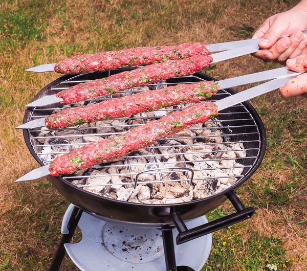 A chef putting red meat shish kebab onto a charcoal barbecue — Stock Photo, Image