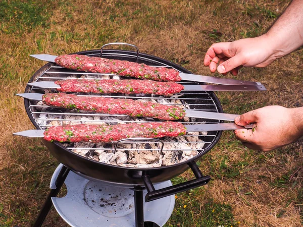 Um chef colocando carne vermelha shish kebab em um churrasco de carvão — Fotografia de Stock