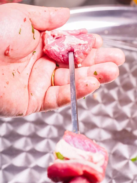 Closeup of a chef entering pieces of meat onto a skewer, making