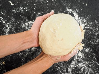 Person holding a proven dough over black table with flour mess clipart