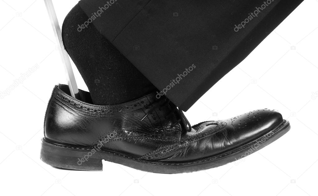 Person wearing black suit and socks entering foot into black leather shoes with shoehorn