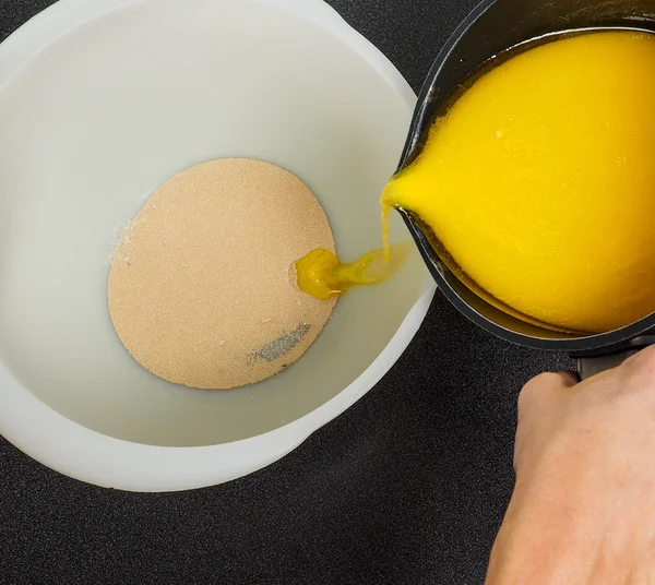 Mano vertiendo mantequilla derretida en un tazón con levadura seca — Foto de Stock