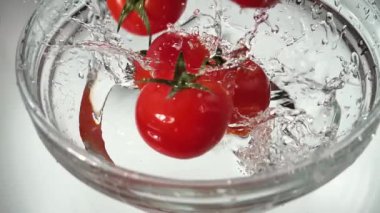 Kırmızı domatesler yavaşça bir tabak suya düşüyorlar.