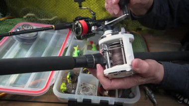 Stüdyo kompozisyonunda bir masada spor balıkçılık ekipmanları, bir ağın arka planına karşı. Balıkçının elleri, olta takımını kontrol eder..