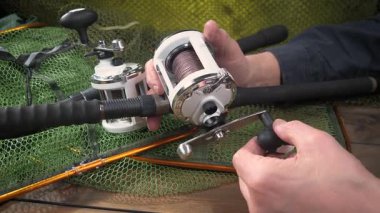 Stüdyo kompozisyonunda bir masada spor balıkçılık ekipmanları, bir ağın arka planına karşı. Balıkçının elleri, olta takımını kontrol eder..