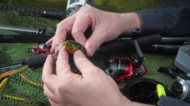 Stüdyo kompozisyonunda bir masada spor balıkçılık ekipmanları, bir ağın arka planına karşı. Balıkçının elleri, olta takımını kontrol eder..