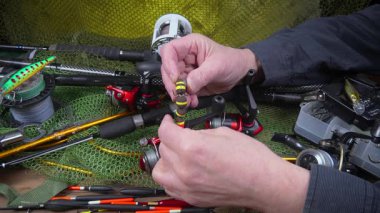 Stüdyo kompozisyonunda bir masada spor balıkçılık ekipmanları, bir ağın arka planına karşı. Balıkçının elleri, olta takımını kontrol eder..