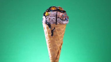 Gözleme külahında çikolatalı dondurma, şurupla ıslatılmış ve parlak renkli bir arka planda yavaşça dönüyor..