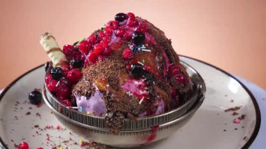 Çikolatalı dondurma kadehleri çikolatalı şekerle serpiştiriliyor ve canlı renkli bir arka planda yavaşça dönüyorlar..