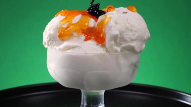 Bir cam kasede vanilyalı dondurma, çikolatalı şekerleme serpiştirilmiş ve parlak renkli arka planda yavaşça dönüyor..