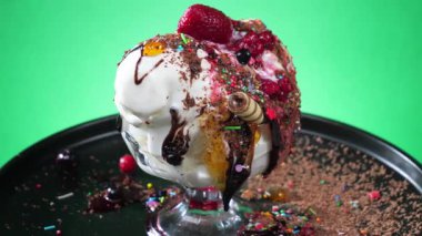 Çikolatalı şekerle kaplı cam kasede çikolatalı dondurma topları, erir ve parlak renkli bir arka planda yavaşça döner..