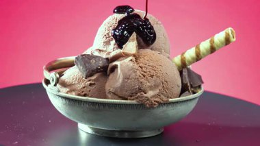 Çikolatalı dondurma kadehleri çikolatalı şekerle serpiştiriliyor ve canlı renkli bir arka planda yavaşça dönüyorlar..