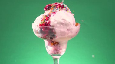Bir bardakta vanilyalı dondurma, şekerle serpilmiş, parlak renkli bir arka planda yavaşça dönüyor..