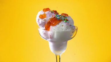 Bir bardakta vanilyalı dondurma, şekerle serpilmiş, parlak renkli bir arka planda yavaşça dönüyor..