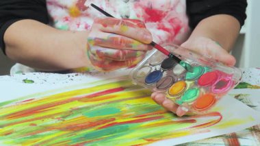 Sanatçının elleri, sanatta yaratıcı imgeler yaratmak için çalışır. Resim boyaları ve fırçalar, palet, guaj ve suluboya kullanarak tuvale çok renkli dokunuşlar uyguluyorlar..