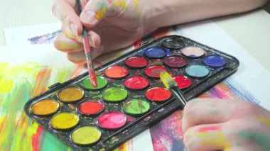 Sanatçının elleri, sanatta yaratıcı imgeler yaratmak için çalışır. Resim boyaları ve fırçalar, palet, guaj ve suluboya kullanarak tuvale çok renkli dokunuşlar uyguluyorlar..