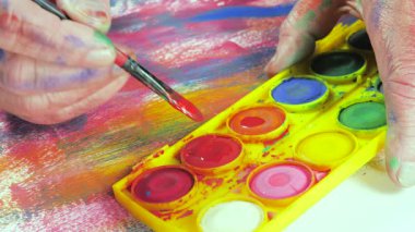 Sanatçının elleri, sanatta yaratıcı imgeler yaratmak için çalışır. Resim boyaları ve fırçalar, palet, guaj ve suluboya kullanarak tuvale çok renkli dokunuşlar uyguluyorlar..