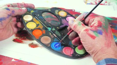 Sanatçının elleri, sanatta yaratıcı imgeler yaratmak için çalışır. Resim boyaları ve fırçalar, palet, guaj ve suluboya kullanarak tuvale çok renkli dokunuşlar uyguluyorlar..