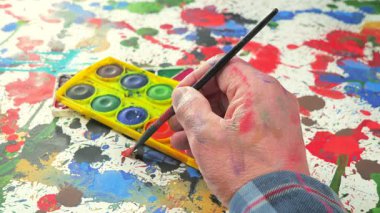 Sanatçının elleri, sanatta yaratıcı imgeler yaratmak için çalışır. Resim boyaları ve fırçalar, palet, guaj ve suluboya kullanarak tuvale çok renkli dokunuşlar uyguluyorlar..