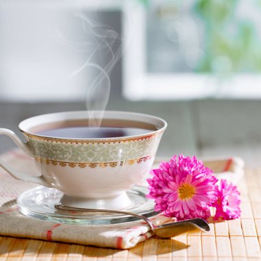 Hafif ahşap zemin üzerinde bir fincan buharlı çay, masada aksesuarlarla birlikte. Metin için boşluk.
