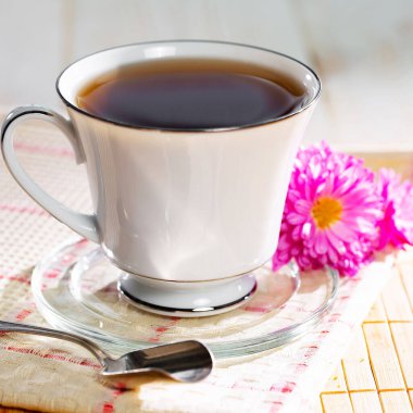 Hafif ahşap zemin üzerinde bir fincan buharlı çay, masada aksesuarlarla birlikte. Metin için boşluk.