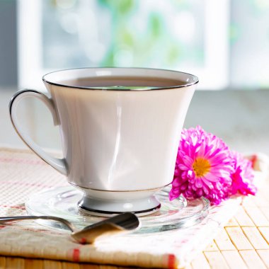 Hafif ahşap zemin üzerinde bir fincan buharlı çay, masada aksesuarlarla birlikte. Metin için boşluk.