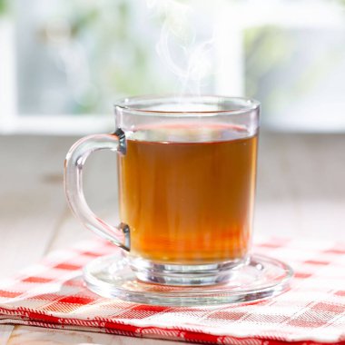 Hafif ahşap zemin üzerinde bir fincan buharlı çay, masada aksesuarlarla birlikte. Metin için boşluk.