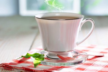 Bir fincan buharlı çay, hafif ahşap arka plan, masada aksesuarlarla kompozisyon..