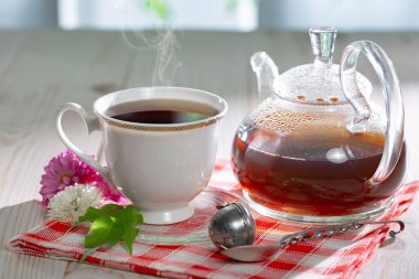 Hafif arkaplanlı çaydanlıklı bir fincan çay, masada aksesuarları olan bir kompozisyon. Metin için boşluk.