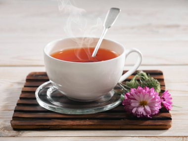 Bir fincan buharlı çay, hafif ahşap arka plan, masada aksesuarlarla kompozisyon..