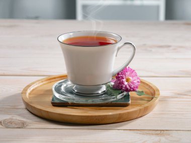Bir fincan buharlı çay, hafif ahşap arka plan, masada aksesuarlarla kompozisyon..