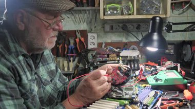 Yaşlı bir teknisyen, ölçüm aletleri ve teknik aletlerle atölyede bilgisayar donanımı tamir ediyor. Yavaş çekim.