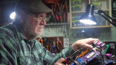 Yaşlı bir teknisyen, ölçüm aletleri ve teknik aletlerle atölyede bilgisayar donanımı tamir ediyor. Yavaş çekim.