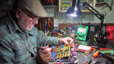 Yaşlı bir teknisyen, ölçüm aletleri ve teknik aletlerle atölyede bilgisayar donanımı tamir ediyor. Yavaş çekim.