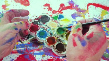 Bir sanatçı fırçaya suluboya boya uygular. Ellerine yakın çekim..