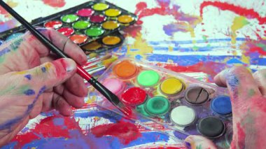 Bir sanatçı bir fırçayla bir tuvale suluboya boya sürer. Ellerine yakın çekim..